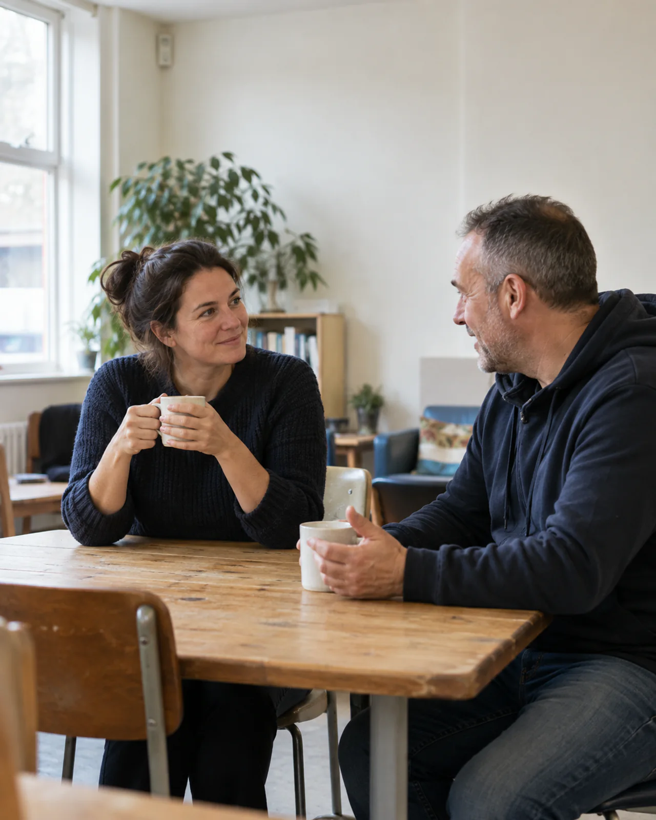 Two adults having a relaxed conversation over tea in a community room